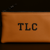 Brown leather pouch with 'TLC' monogram on a black background